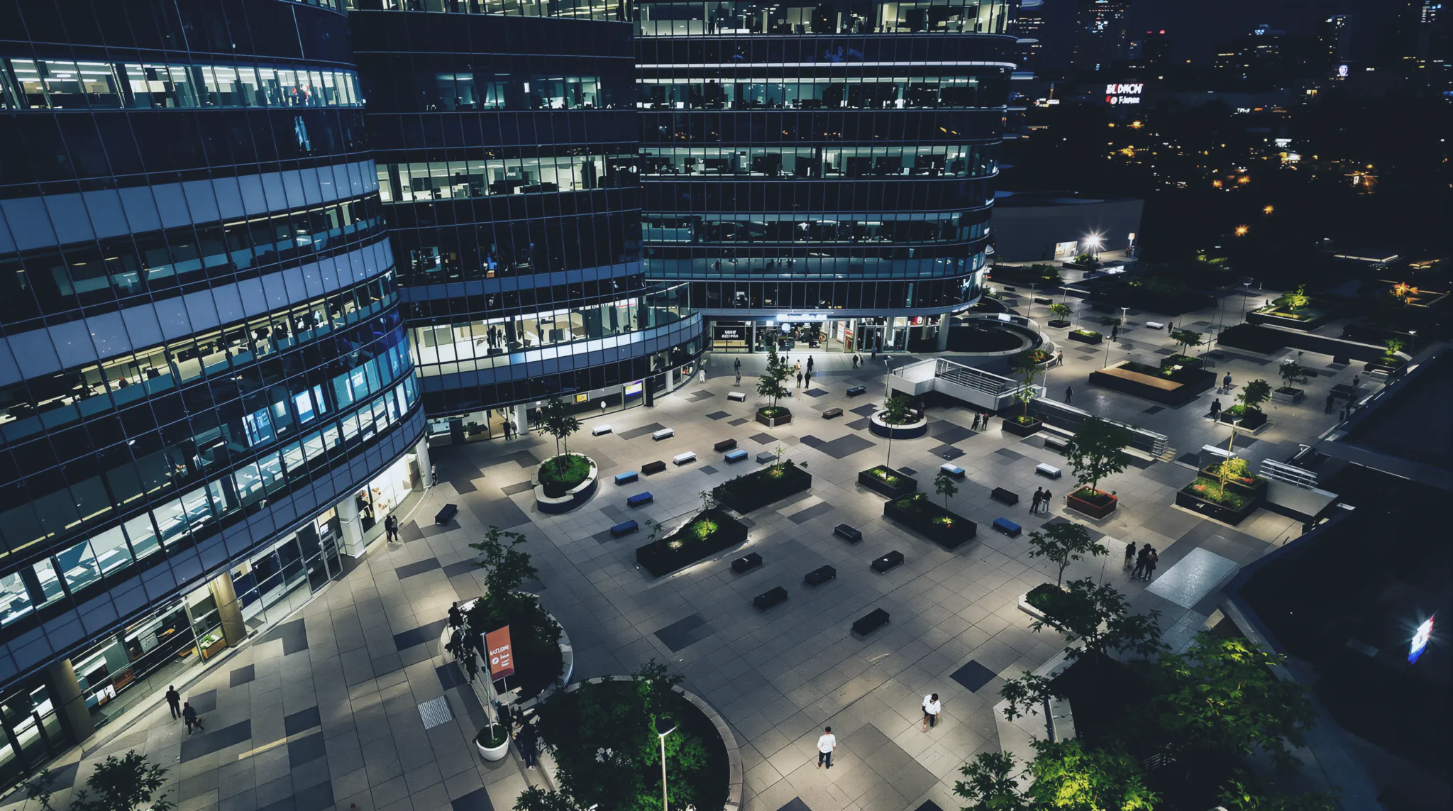 Aerial night view of an office tower and plaza under patrol.